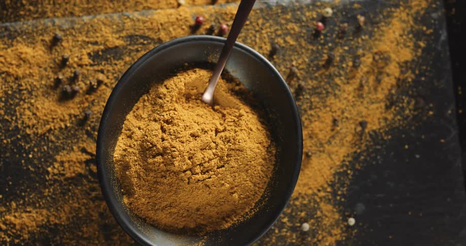 A golden brown powder sits in a bowl and on a table surface