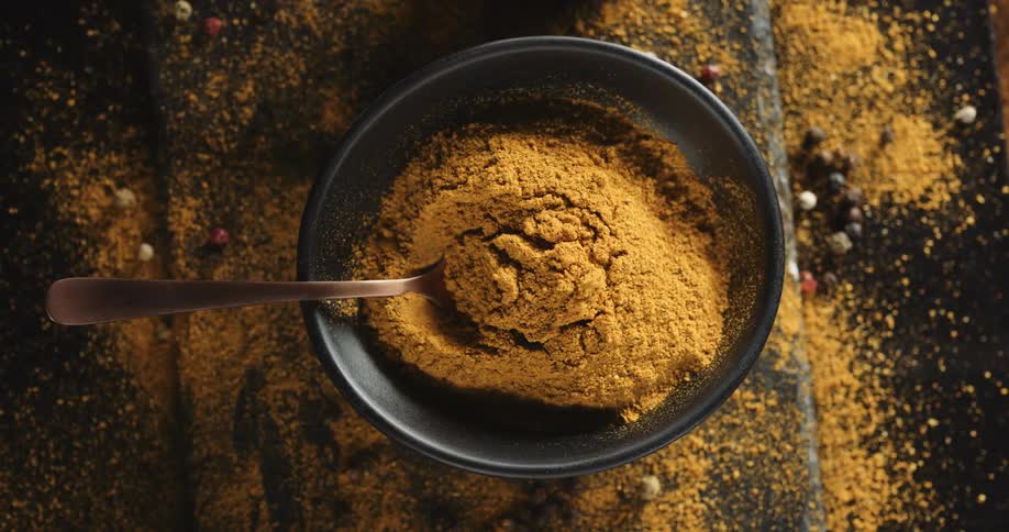 A spoon rests in a bowl filled with a golden powder