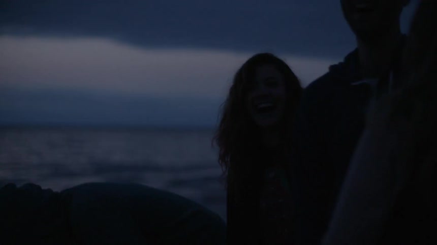 A group of friends laugh and interact on a beach at night