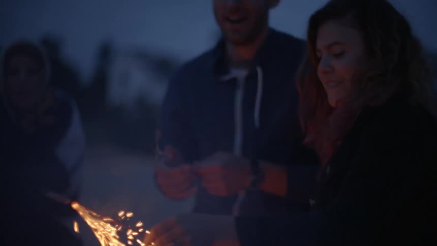A woman lights a firework as others watch