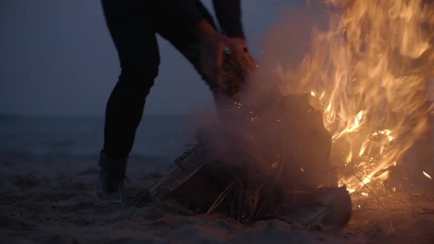 A man puts some tinder in a fire at dawn