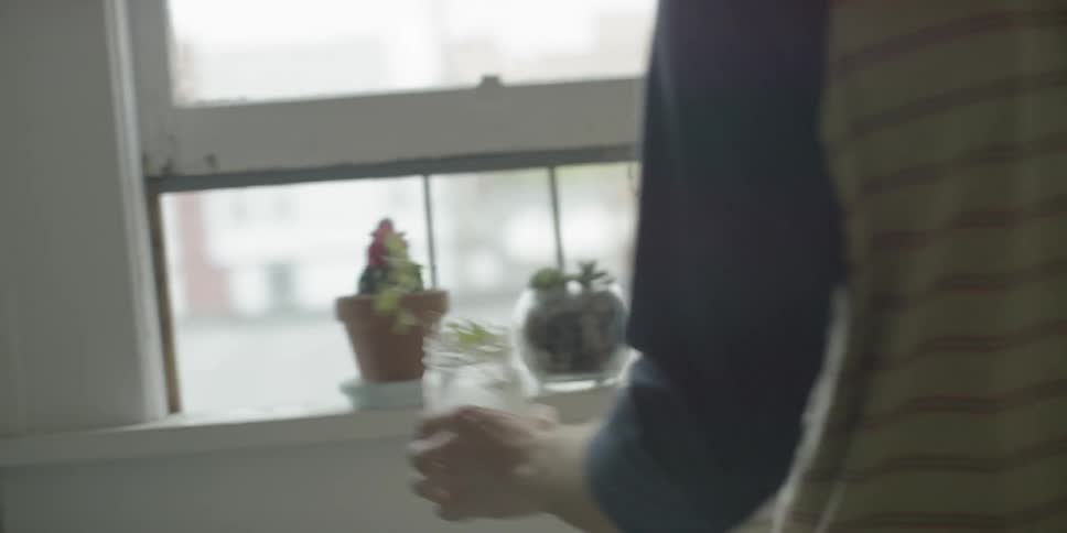 A man runs some water on a plant in a jar
