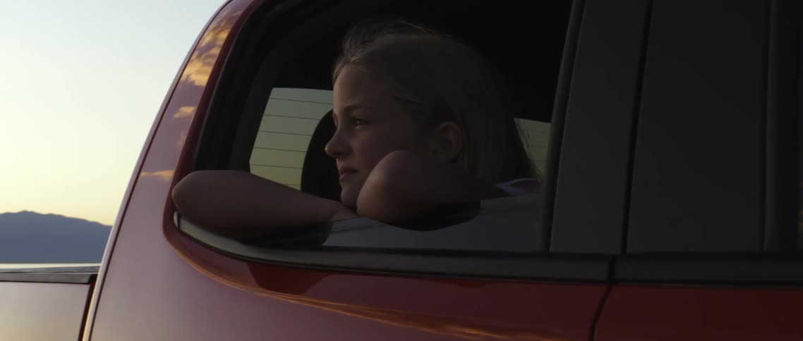 A young girl looking out the open window of a red truck