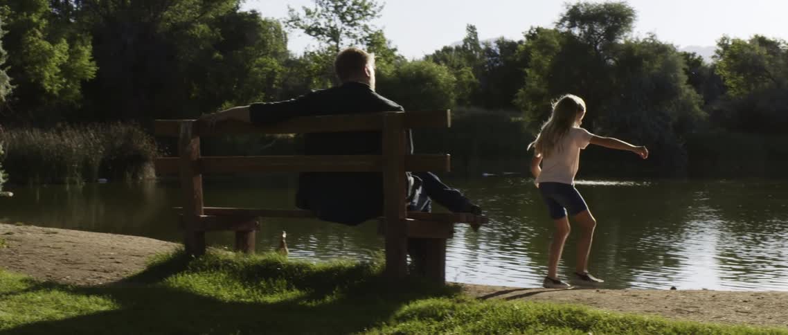 Father and daughter sitting on a bench near a lake in the park at morning