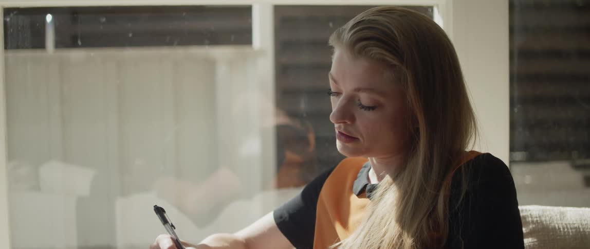 A woman writing while sitting indoors looks up in thought for a moment before continuing to write