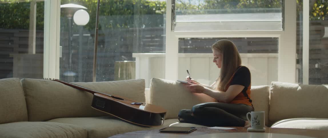 A woman writes in a notebook while sitting on a sofa in the living room of a house during the day