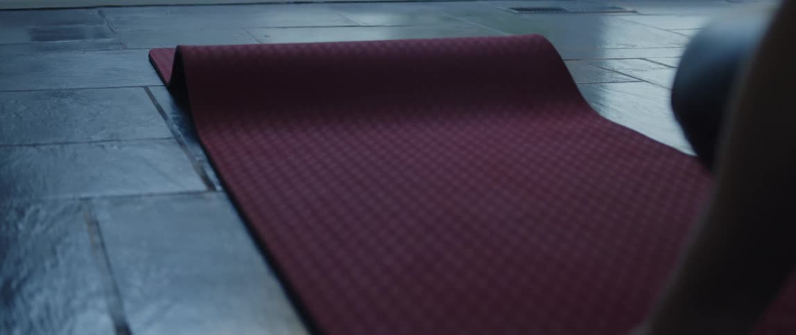 Woman wearing black pants unrolls crimson yoga mat