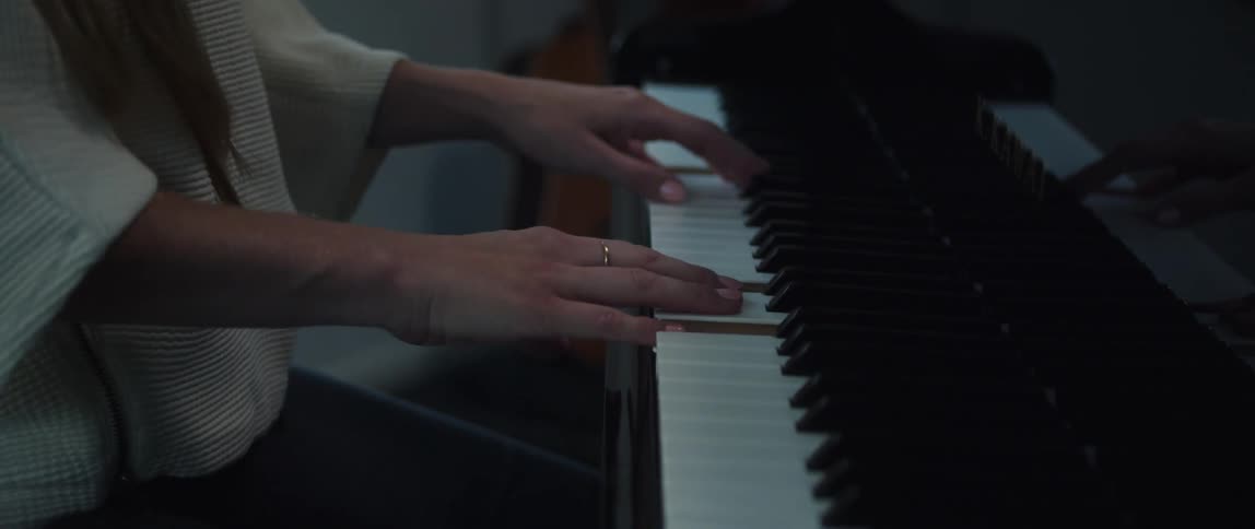 Woman in white sweater and jeans plays grand piano