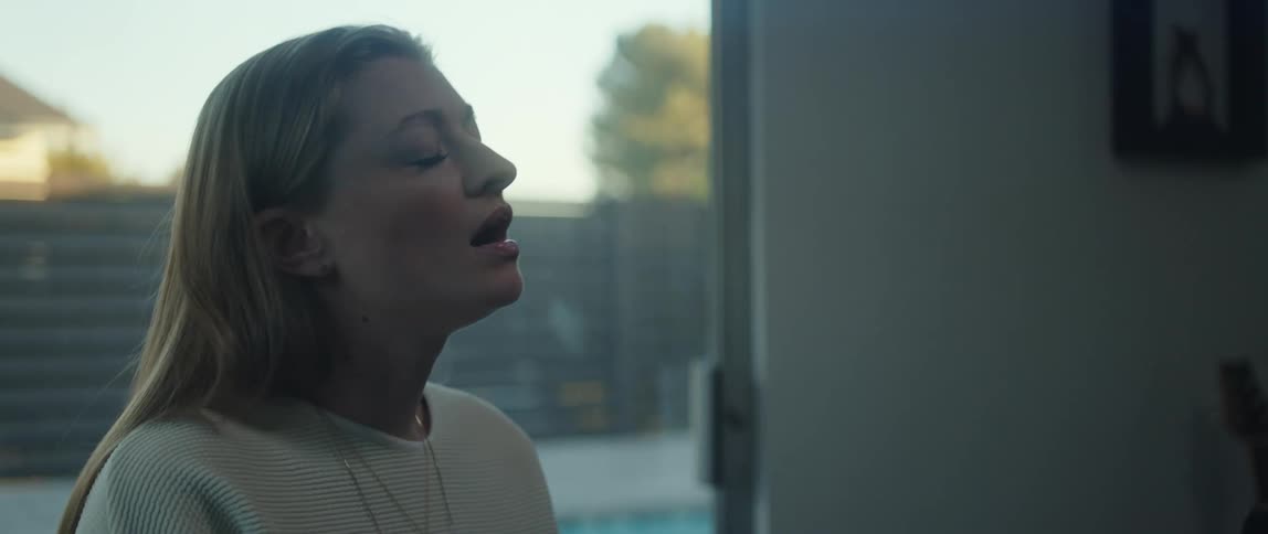 A woman with long hair singing with her eyes closed in front of a glass sliding door