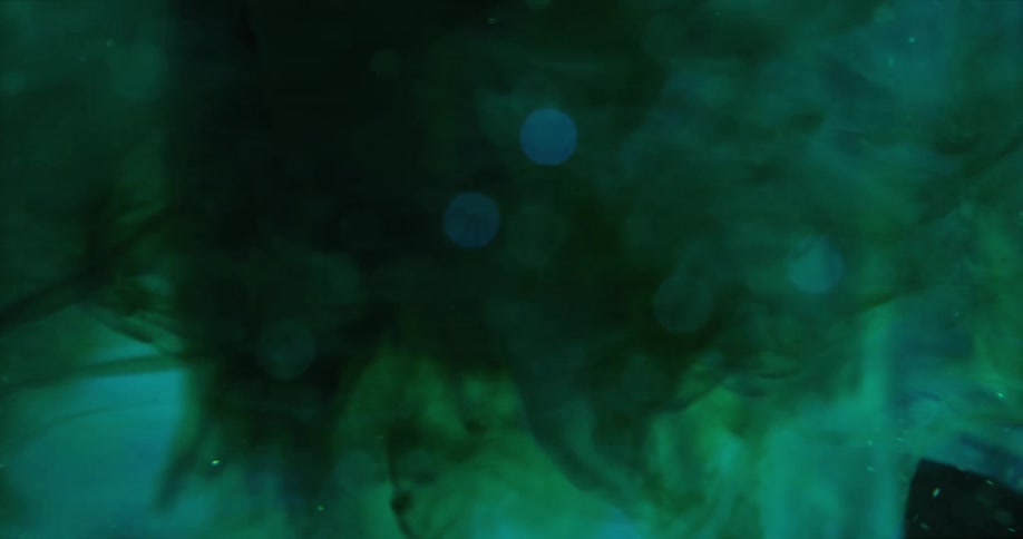 Close up of spinning blobs of green liquid ink suspended in water