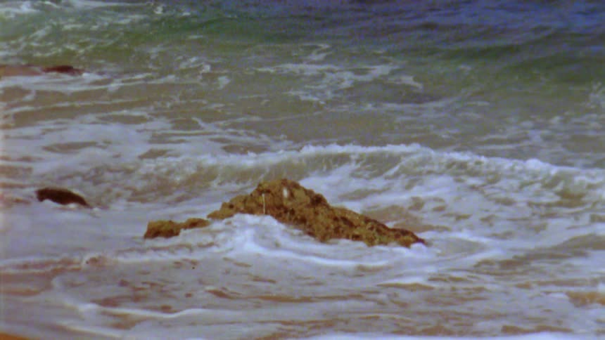 Ocean waves wash round a rock on a sandy beach during the day