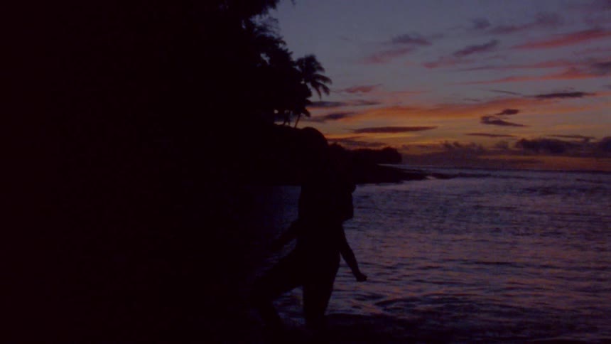 A parent is carrying their child by the coast at dusk