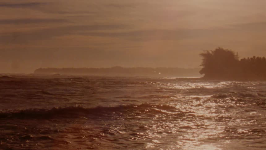 Slow motion footage of golden sunlight reflecting over the waves near the tropical coast