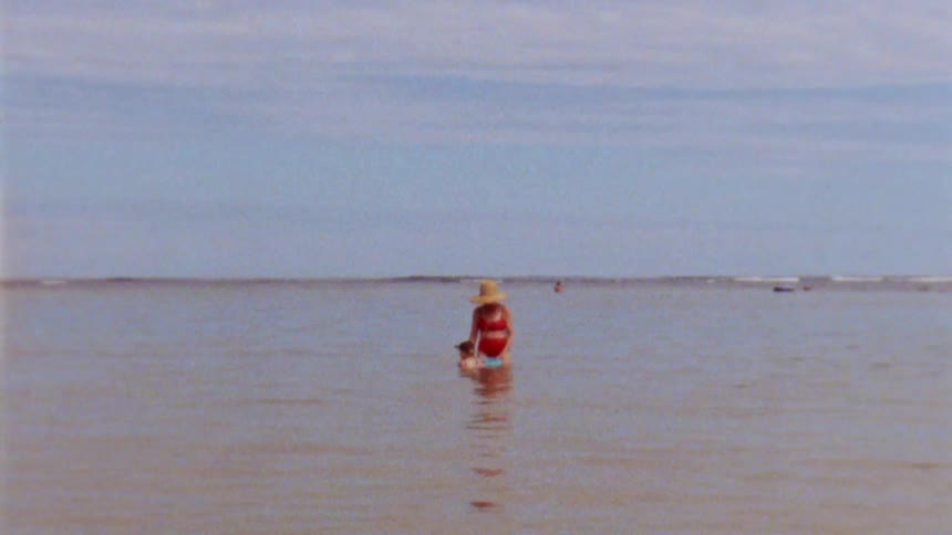 Mother with hat and red bikini plays with her daughter in sea