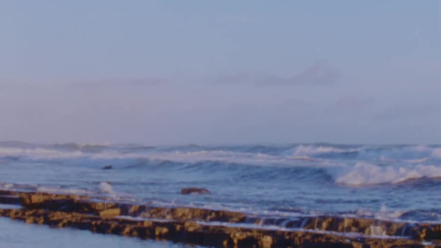 Small calm ocean waves gently crashing on the coast at evening caught on vintage film