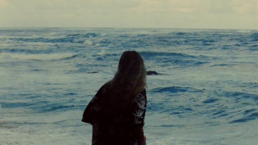 Woman stands looking toward horizon as waves roll toward beach