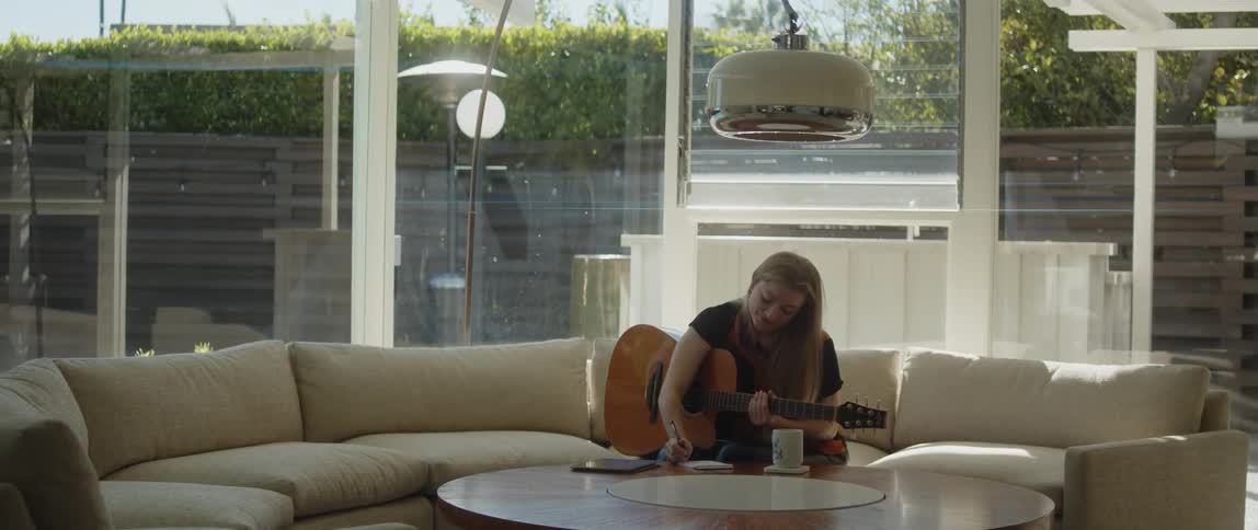 A woman is holding her guitar as she writes