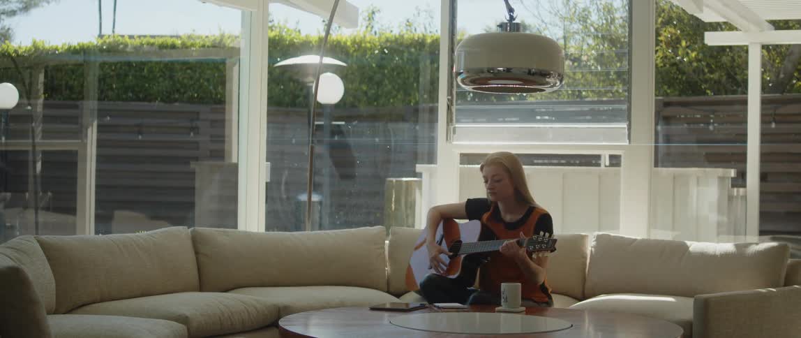 A woman is playing a guitar and sitting indoors