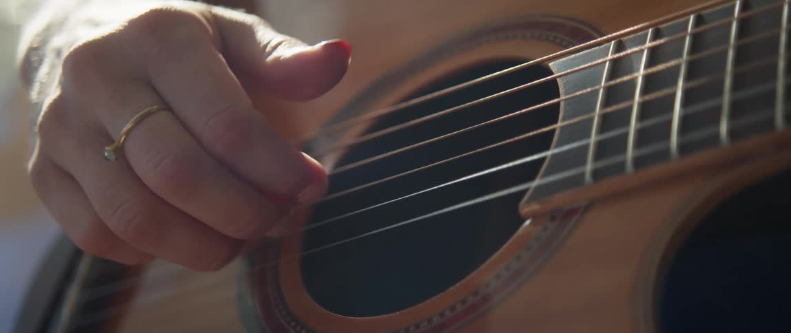 Close up of a woman's hand plucking the strings of an acoustic guitar outdoors