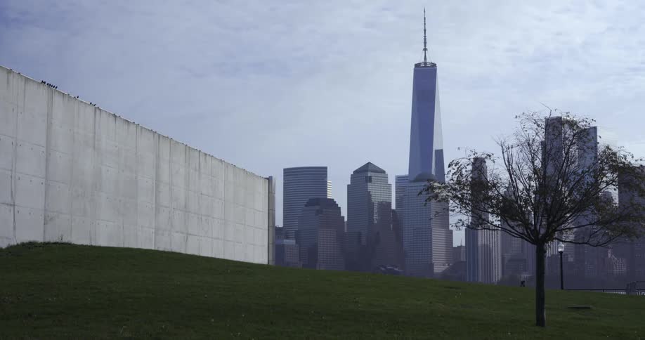 Flock of birds fly near building as people walk through park with city skyscrapers in the background