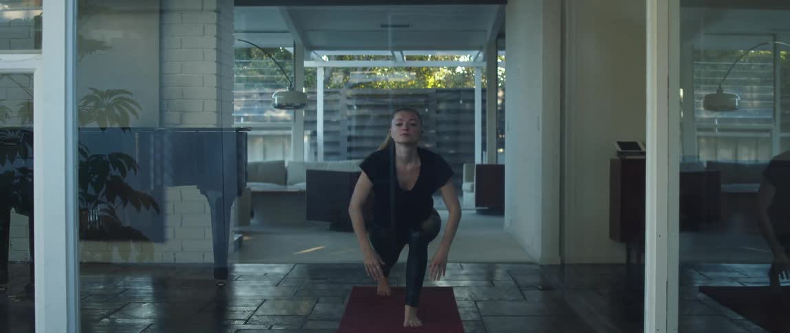 Woman moves through yoga poses in large room near open door