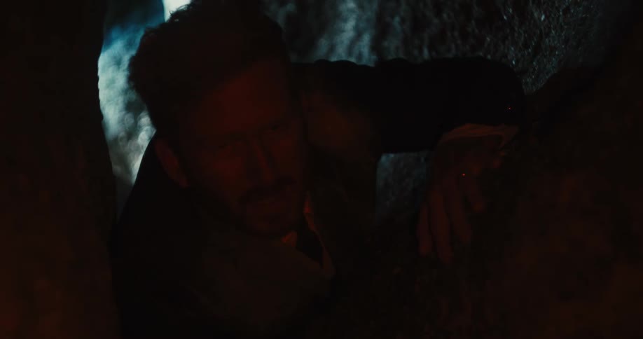 A man is crawling in a tight cave
