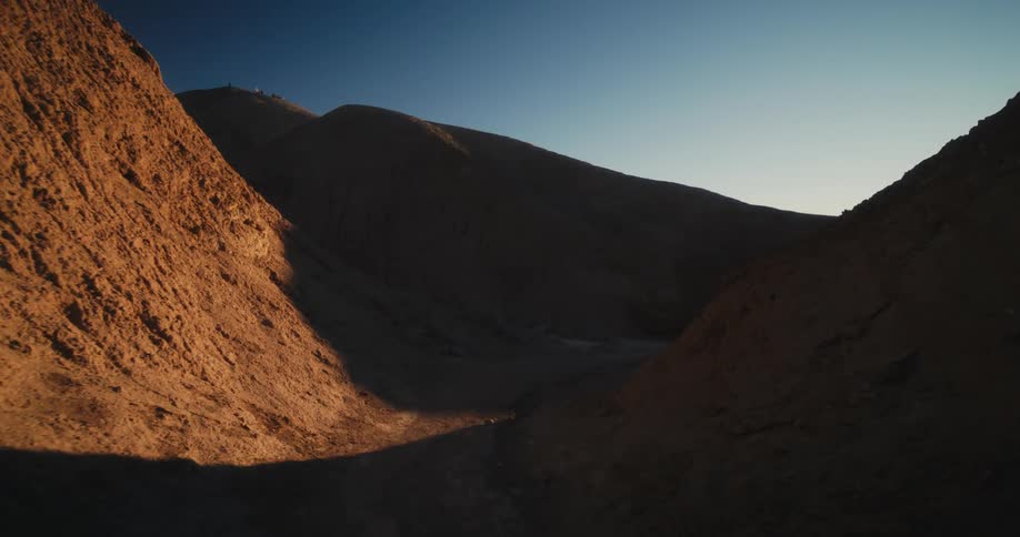 Shadow fills space curving between mountains as sun shines from horizon into space at end of path