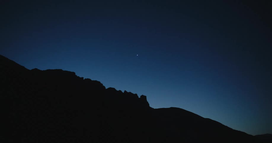 A bright star in a clear sky is above the silhouette of a mountain
