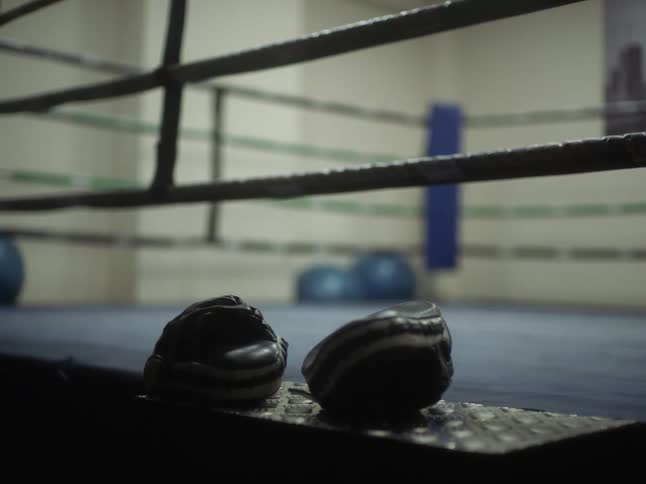 Gloves sit on edge just outside rope of boxing ring