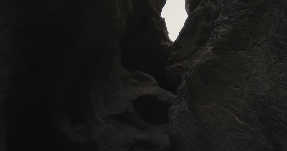 Sky above ocean is visible through narrow opening between cliffs