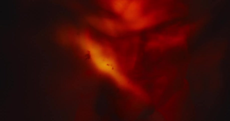 A red light shines on a mans face as he stands in a cave