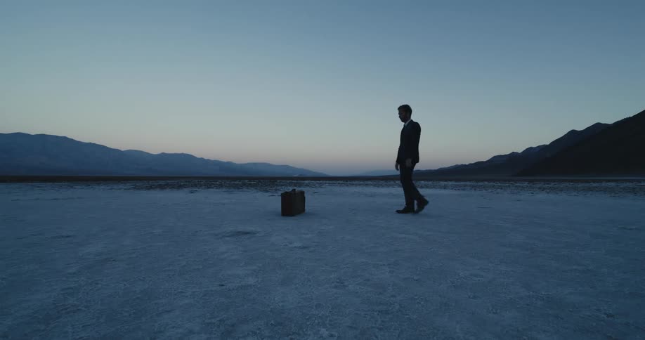 A male wearing a suit is walking towards a briefcase near mountains