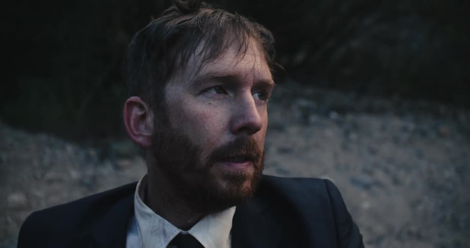 Close up of the face of a soaking wet man wearing a business sitting on the groundion