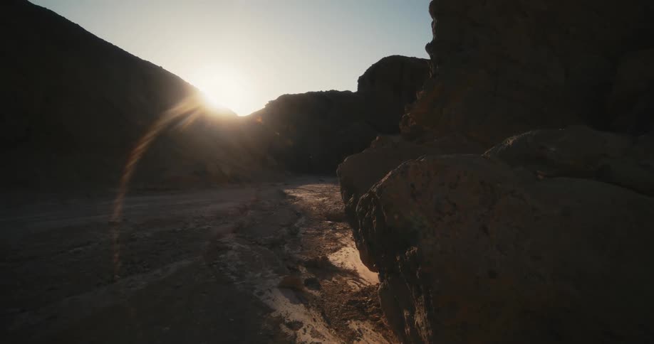 The sun shines brightly over desert mountains in a clear sky