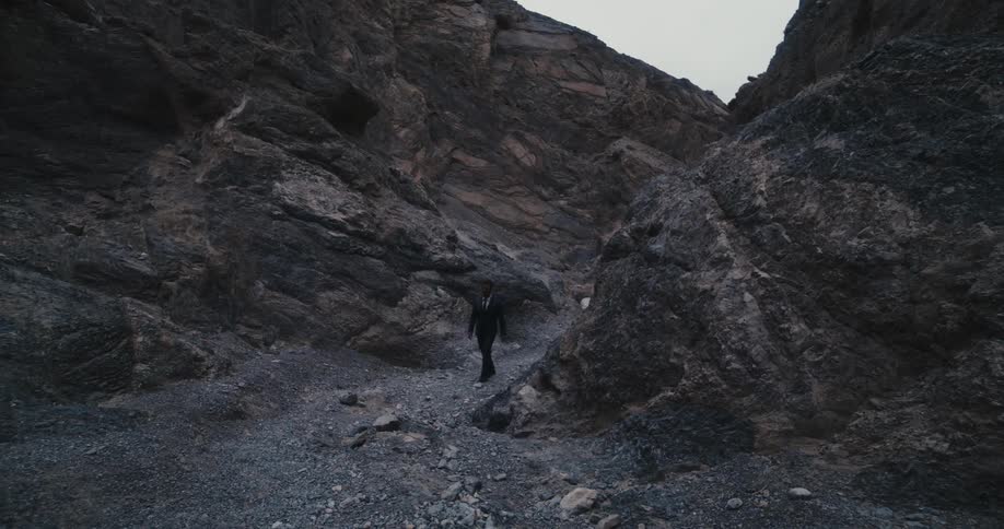 A man in a suit slowly walks through the rubble on a mountain during the day
