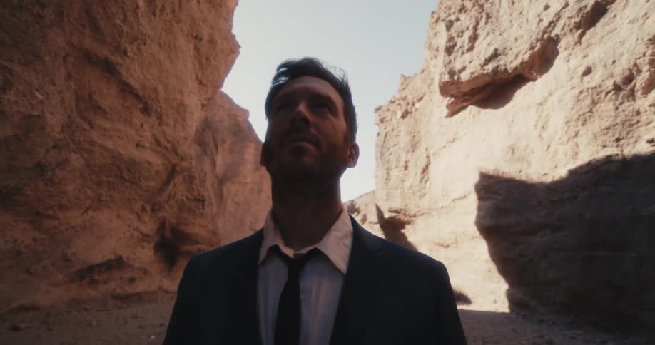A man in a suit looks up at his surroundings while standing in a canyon during the day
