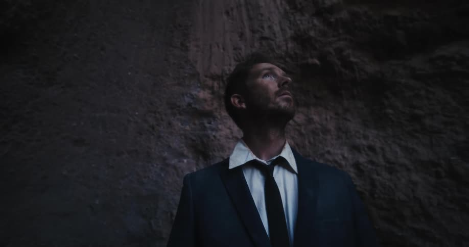 Young disheveled man wearing an unkempt business suit looking up at the bottom of a canyon