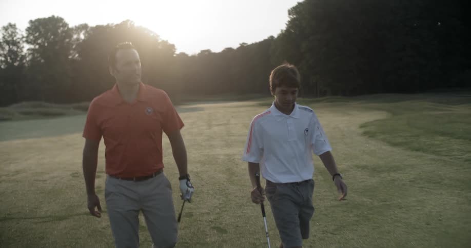 A man and boy walk on a golf course in the evening