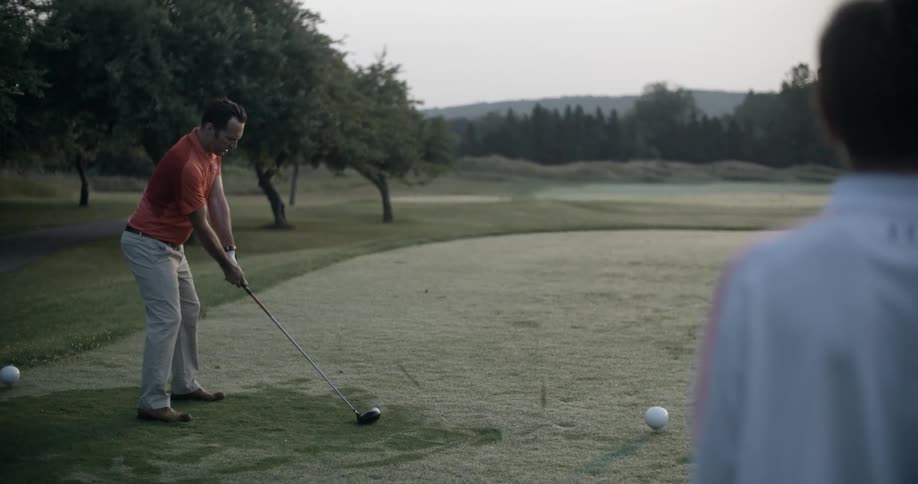 A man plays golf outside while another man watches