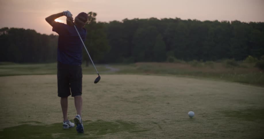 A man is driving golf balls at sunset