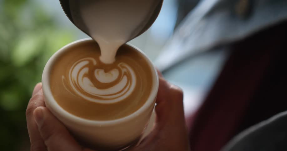 Barista creates foam art with milk on a cup of coffee