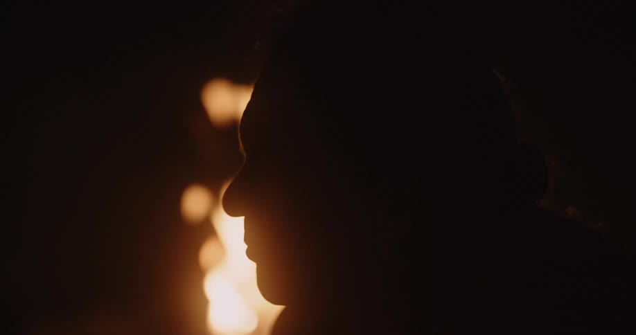 Man silhouetted against campfire raises smoking object up