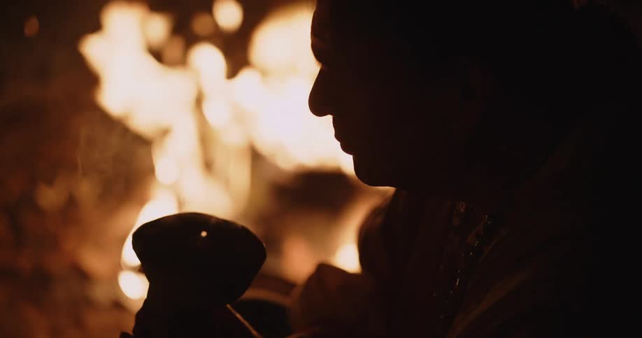 Close up of the silhouette of a native american performing a ritual in front of a bonfire at night