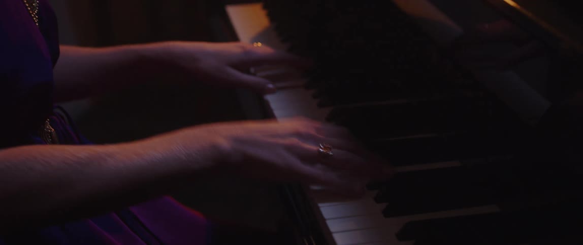 A woman plays the piano in a dimly lit room