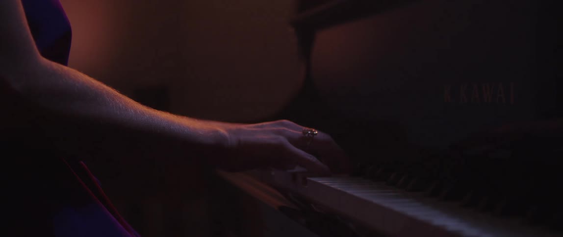 Close up of the hands of a woman playing piano on a dimly lit room