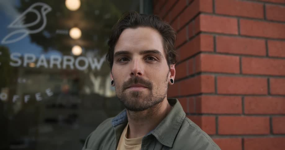 A man sitting in front of a coffee shop turns to look at the camera
