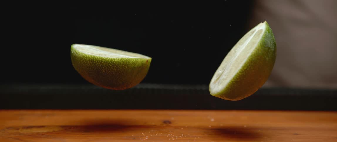 A lime falling onto a wood table and splitting in two
