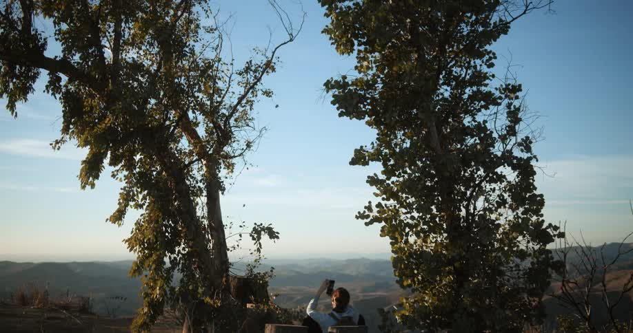 A man holds up a cup while sitting along a cliff