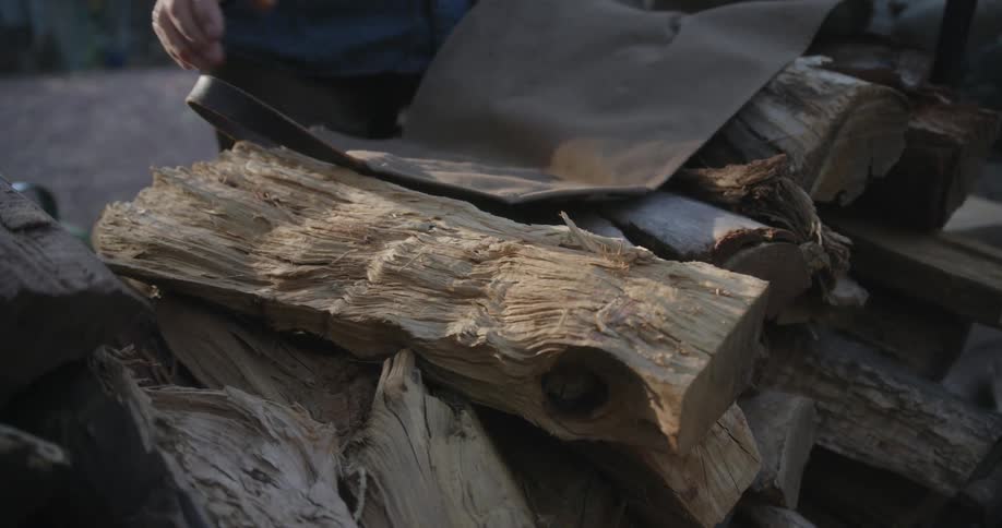 A man is outside and he is picking up some wood