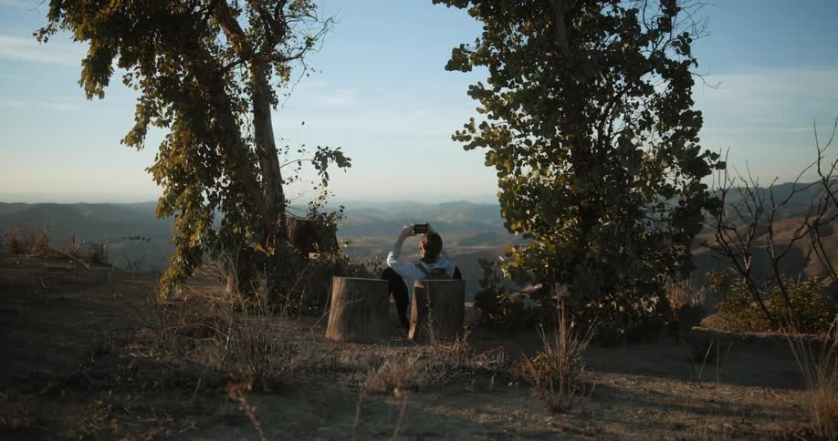 Person sits on ground taking pictures of scenic landscape with their smartphone